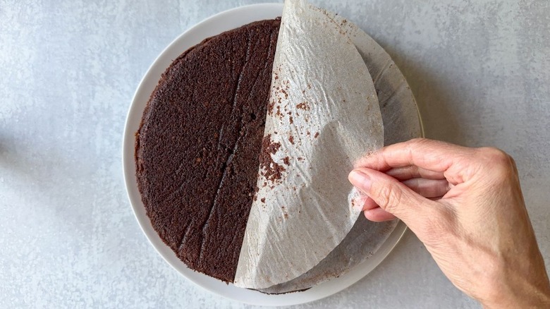 Removing parchment paper from baked flourless Italian gianduja chocolate cake on serving platter