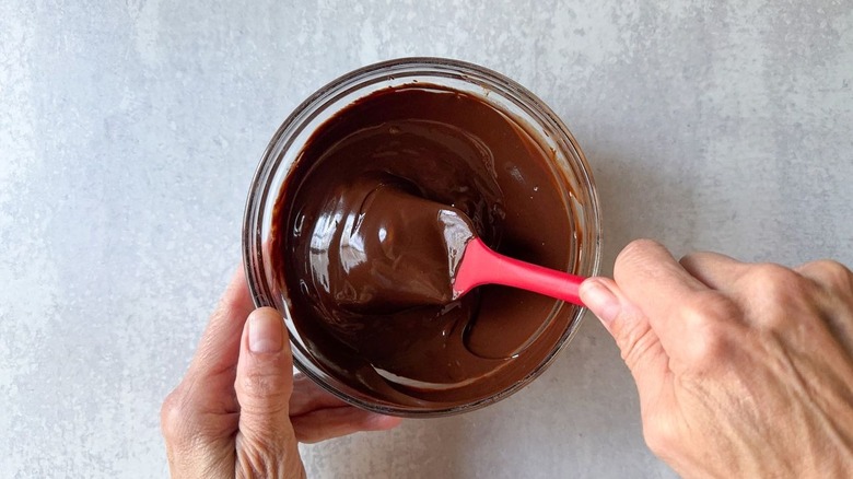 Stirring chocolate glaze in glass bowl with rubber spatula