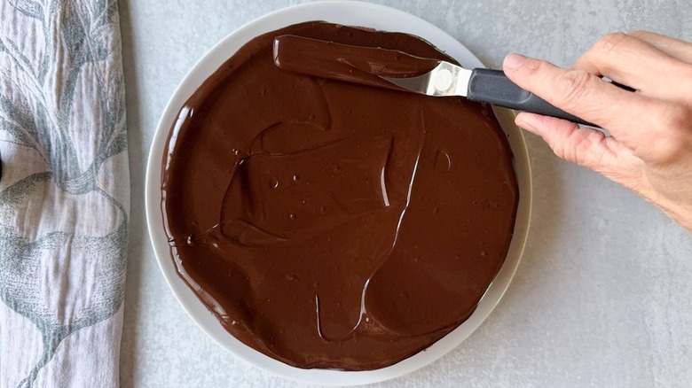 Spreading chocolate glaze over flourless Italian gianduja chocolate cake with offset spatula