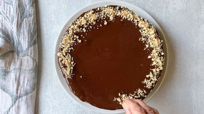 Sprinkling chopped hazelnuts around edge of glazed flourless Italian gianduja chocolate cake