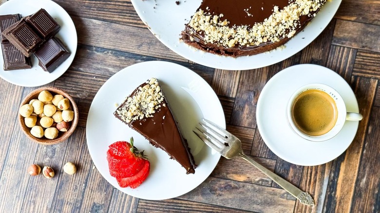 Sliced flourless Italian gianduja chocolate cake on plate with hazelnuts, chocolate, strawberry garnish, and espresso