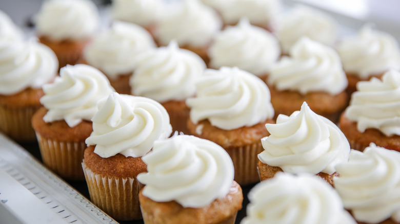 Tray of cupcakes with white buttercream frosting on counter.