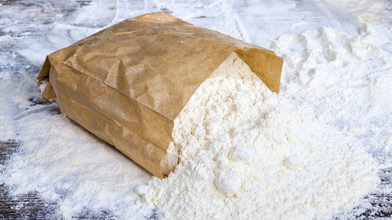 Unmarked bag of flour opened and spreading on table.