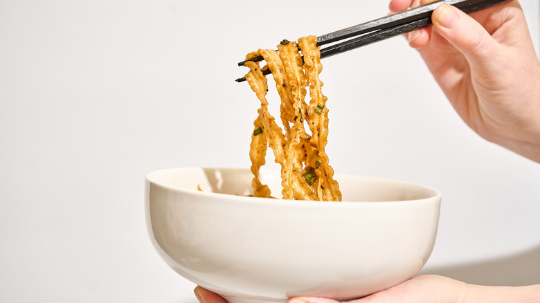 Hand pulling noodles out of a bowl with chopsticks
