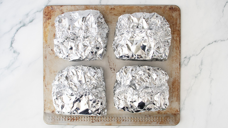 Four parcels of pasta in aluminum foil on a baking sheet