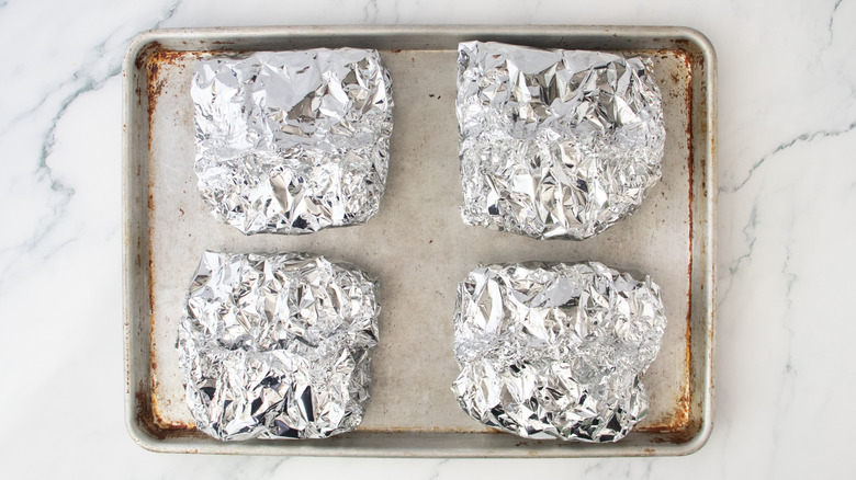 Four grilled parcels of pasta in aluminum foil on a baking sheet