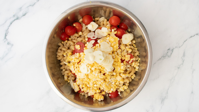 Cooked pasta, fresh corn, and cherry tomatoes in a large bowl