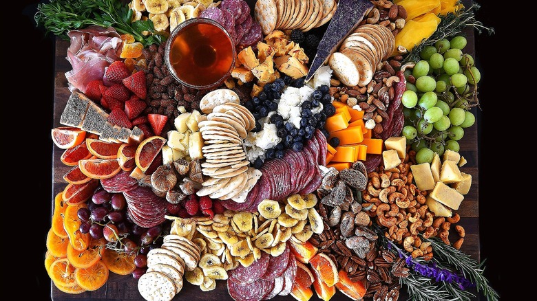 Large rectangular charcuterie board filled with cured meats, nuts, cheeses, and both fresh and dried fruits