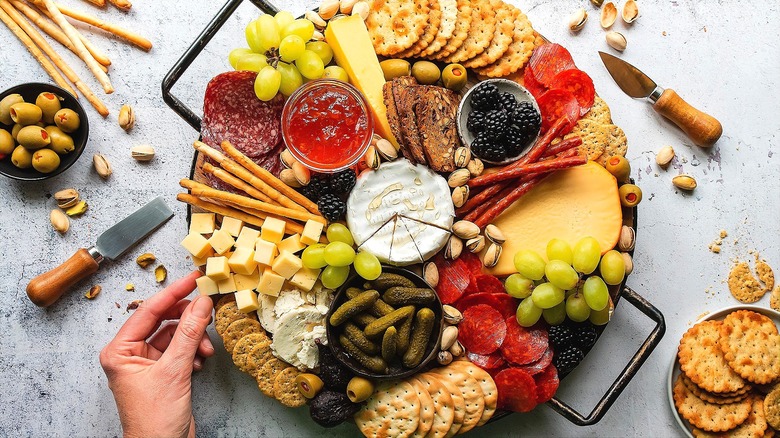 Hand grabbing a cheese cube off of a charcuterie board filled with fruit, cured meats, and crackers