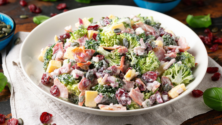 A bowl of cold, mayo-based broccoli salad with bacon, dried cranberries, pumpkin seeds, and cheese.