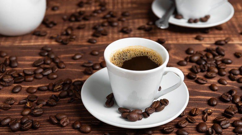 white cup of coffee surrounded by whole beans