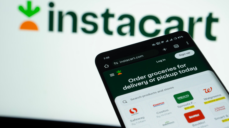 The Instacart website open on a phone in front of the Instacart logo.