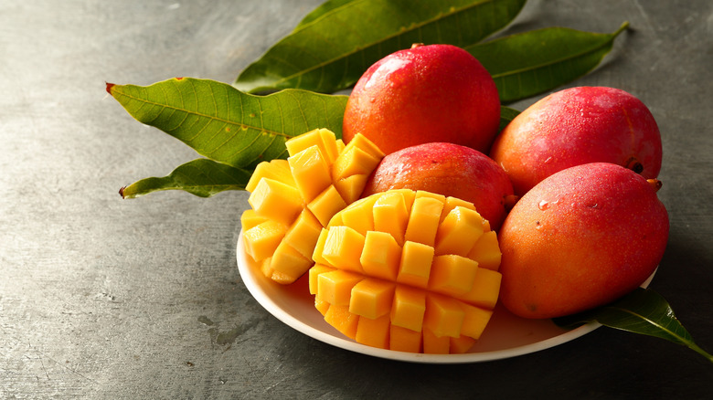 Cubed mango still on skin with several mangoes on a plate