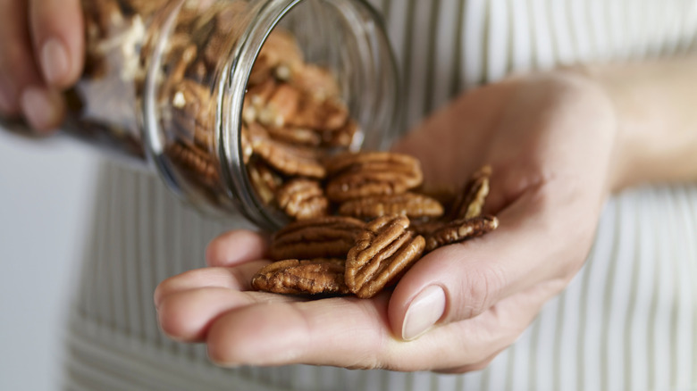Person dumping pecans out of a glass jar and into their hand
