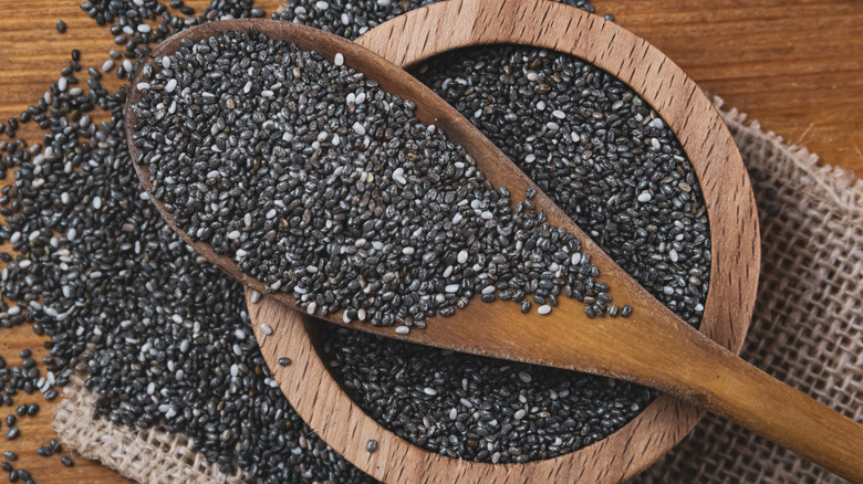 Chia seeds overflowing from a wooden bowl with a wooden spoon
