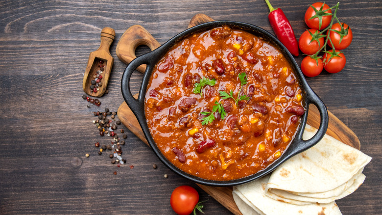 Chili with red kidney beans in a cast iron skillet with tortillas, tomatoes and peppers on the side