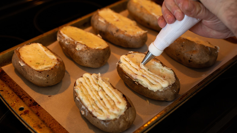 A person's hands are seen piping twice-baked potatoes on a baking sheet