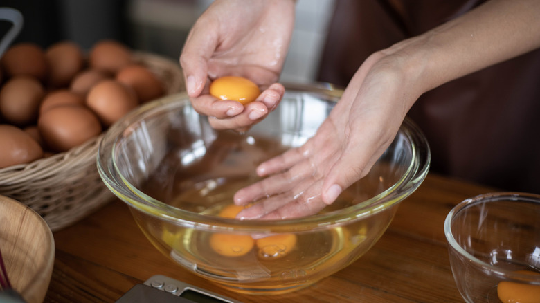 A person's hands are seen separating egg yolks over a glass bowl