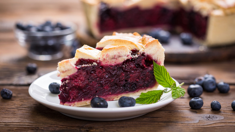 A slice of blueberry pie on a plate with fresh mint leaves on the side