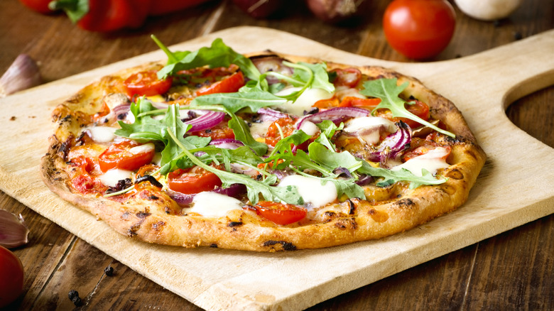A cooked pizza with toppings on a wooden tray.