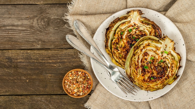 Roasted cabbage steaks on a plate with two forks and a bowl of seasoning on the side