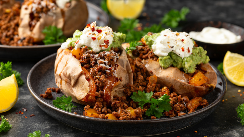 Two loaded baked sweet potatoes with carne asada, guacamole, sour cream, cheese, and cilantro on black dish
