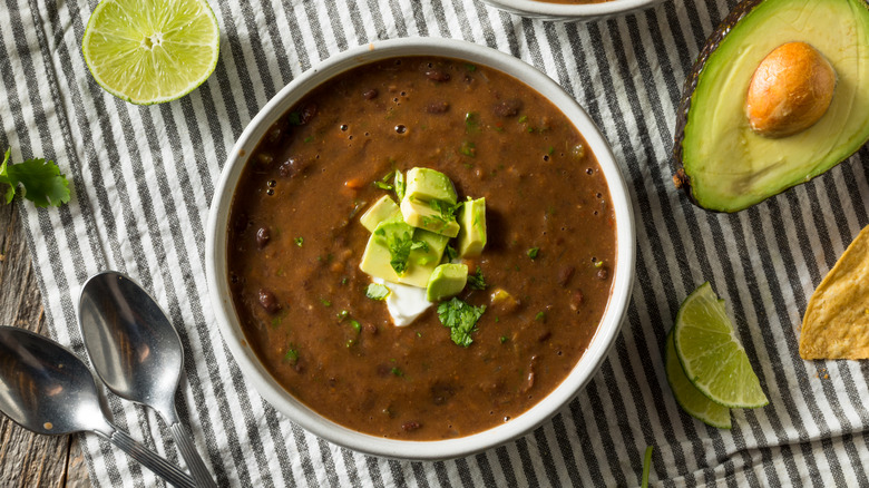 Top view of a bowl of bean soup topped with avocado, sour cream, and cilantro