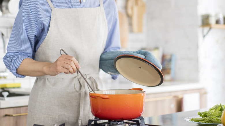 Person ladling soup from orange ceramic pot