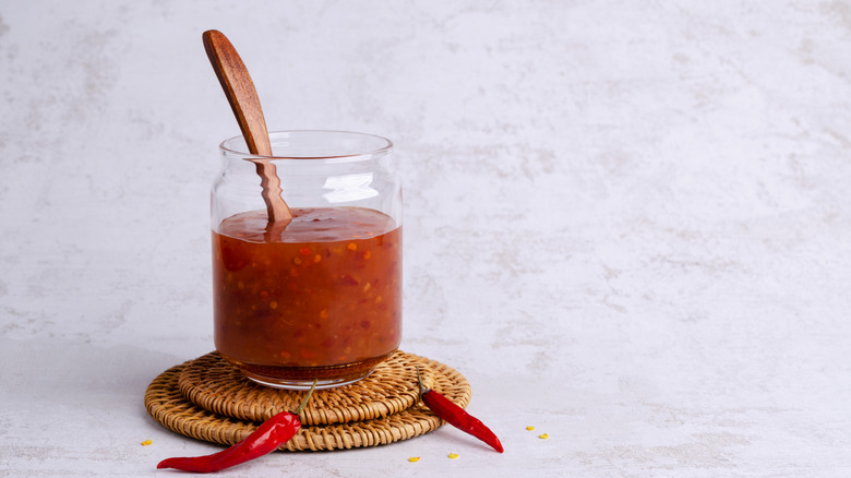 A homemade sweet chili sauce in a glass container with two chilies next to it