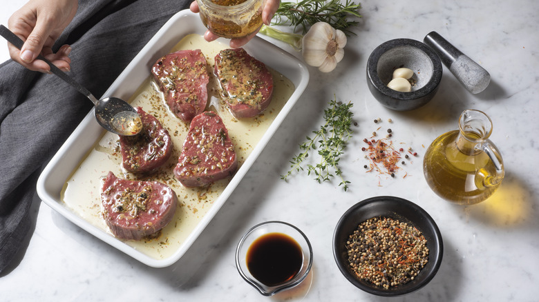 Steak in marinade, with a person spooning over remaining marinade