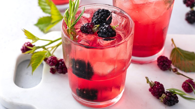 Pink-tinted cocktail with fresh blackberries, rosemary, and ice in a clear glass.