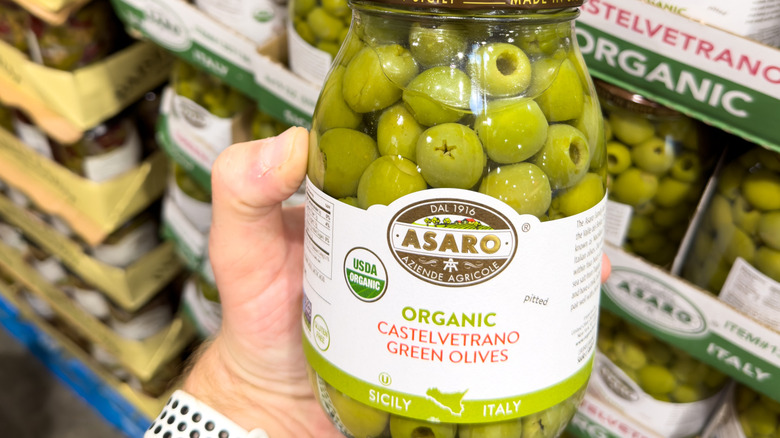 Person's hand holding a jar of pitted Castelvetrano olives