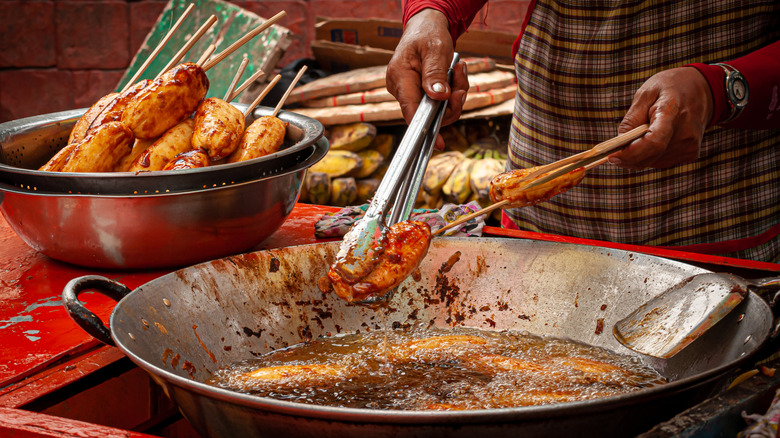 A street vendor skewering banana cue on top of a used pan filled with oil