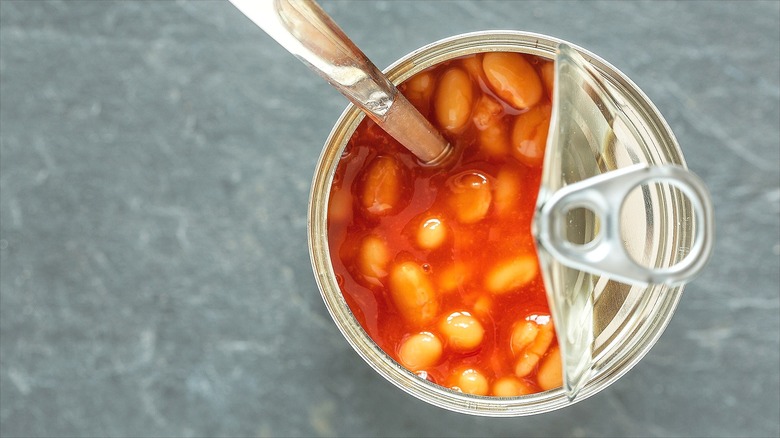 Top-down view of an open can of baked beans with a silver spoon