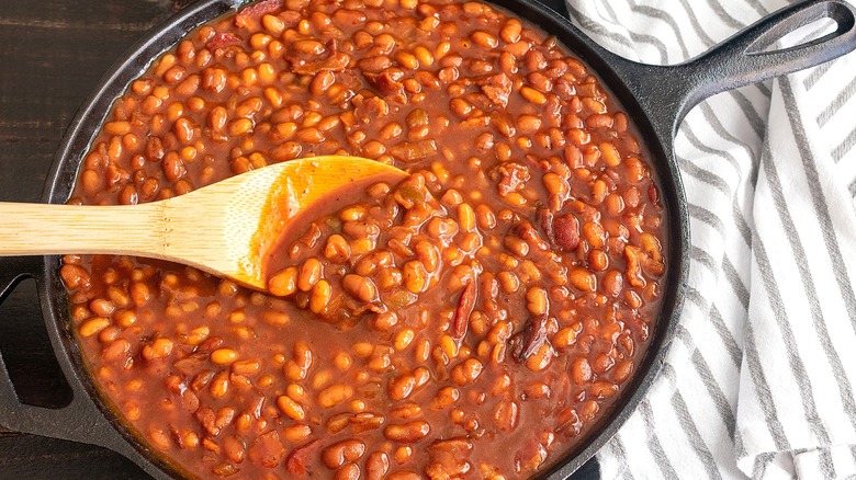 Baked beans with pork in a large cast iron skillet with a wooden spoon