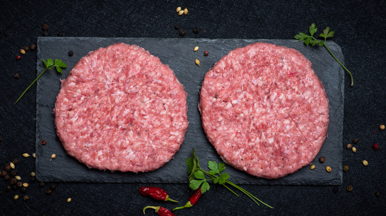 Two homemade raw ground beef patties on a slab.
