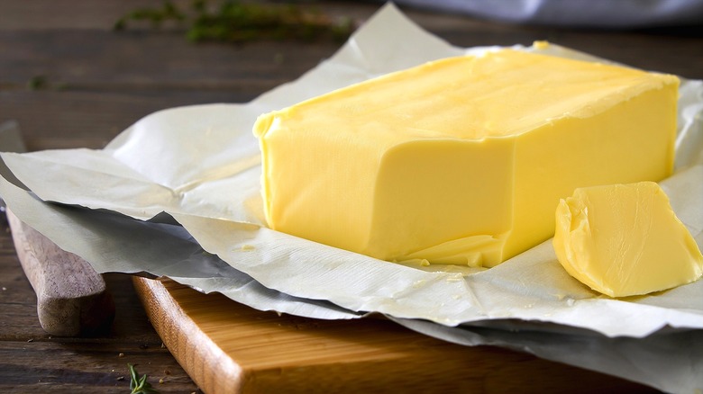 Block of yellow butter over butter paper on a wooden board