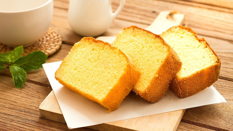 Three slices of golden pound cake over a thick piece of white paper on a wooden serving board