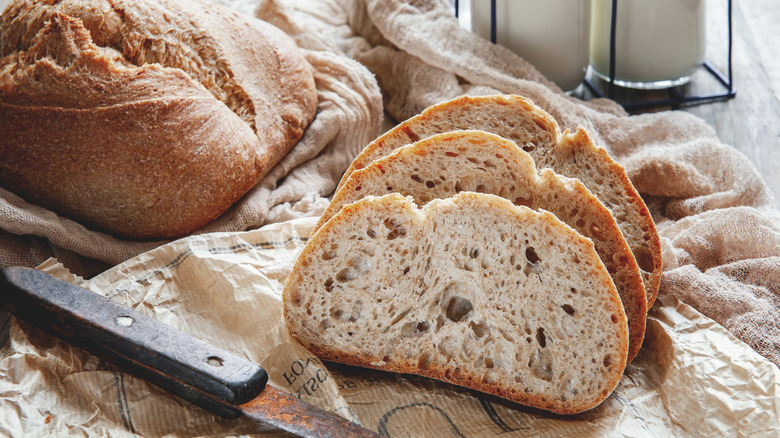 A whole loaf of fresh bread is photographed near a trio of slices.