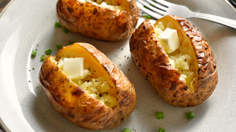 Close up view of oven baked potato with butter and spice on white plate.