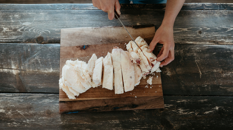 An individual slicing beef tallow with a knife on a wooden board.