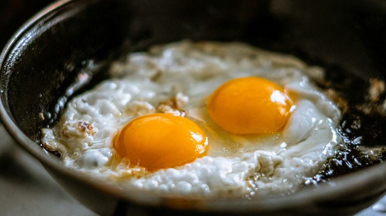 Two eggs frying in a pan with oil.