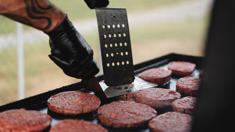 Several burgers are seen cooking on a flattop grill.