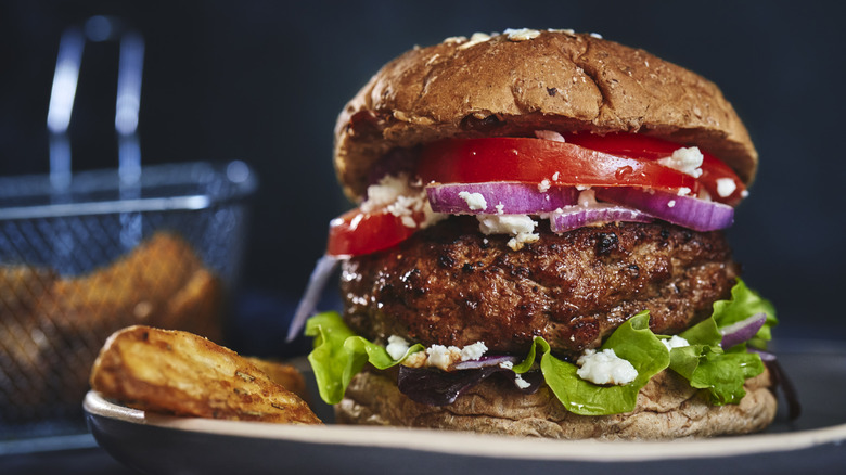 A nicely charred burger on a bun with lettuce, tomato, and onion.