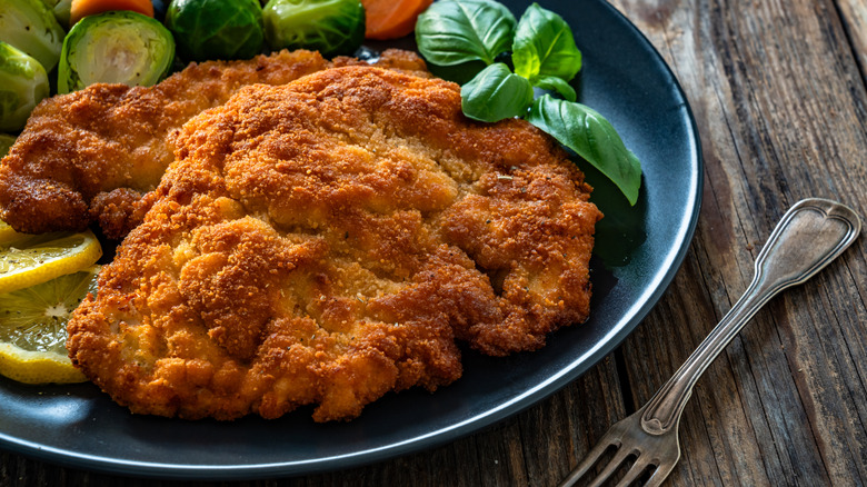 Golden fried pork chops on a blue plate beside a silver fork.