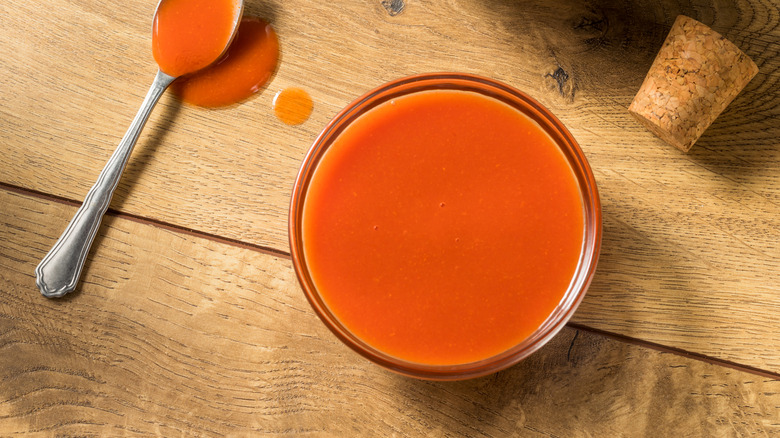 A bowl of bright orange/red Buffalo sauce on a wooden table.