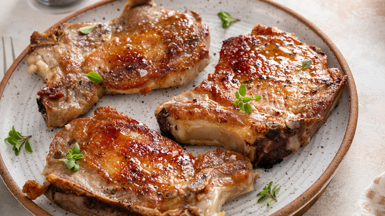 Cooked pork chops on ceramic plate garnished with fresh herbs on table.