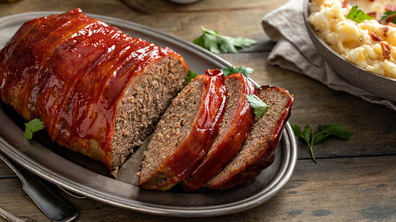 Plate of sliced meatloaf with a glaze and topped with fresh herbs