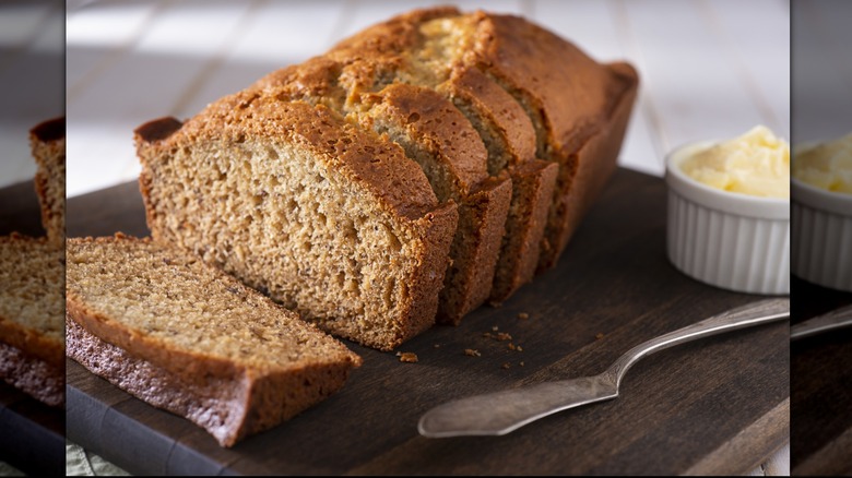 Sliced banana bread on a wooden cutting board with a dish of butter