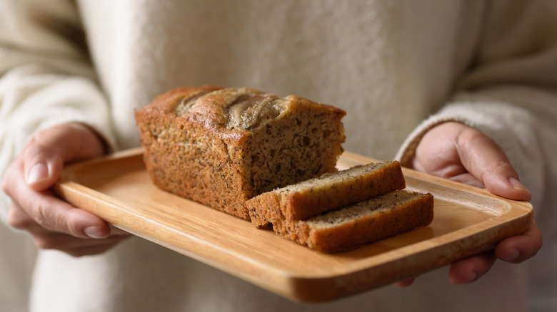 Person holding sliced banana bread on a wooden cutting board